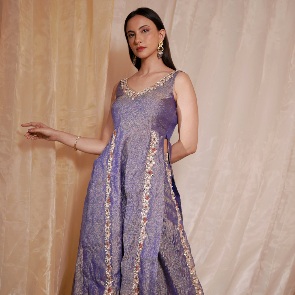 Woman wearing a purple traditional outfit with gold embroidery against a beige curtain background